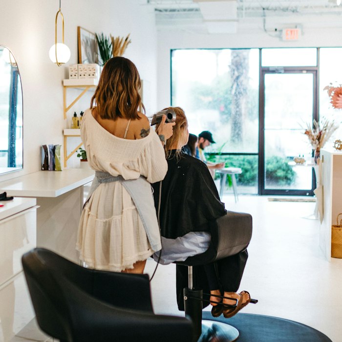 A stylist finishing a blow-dry in a bright, plant-filled salon.