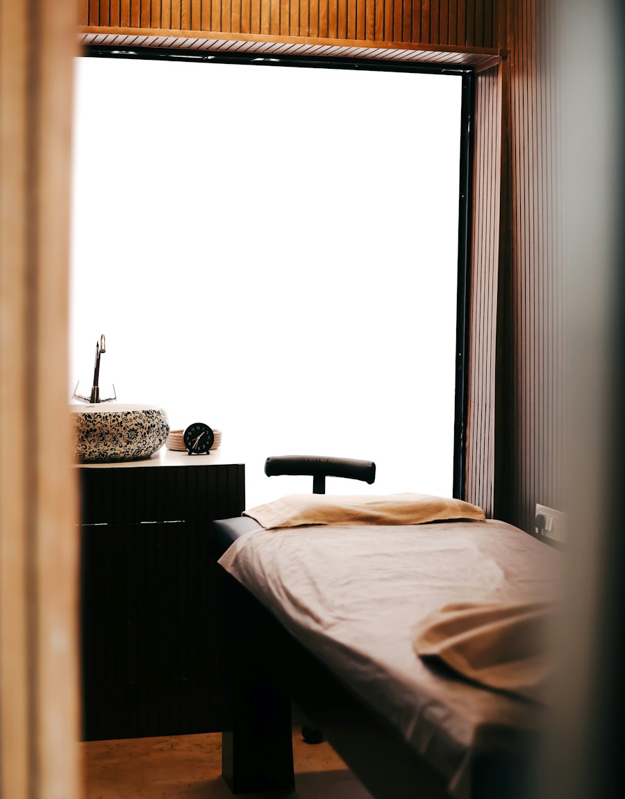 A quiet treatment room with a linen-covered bed beside a window.