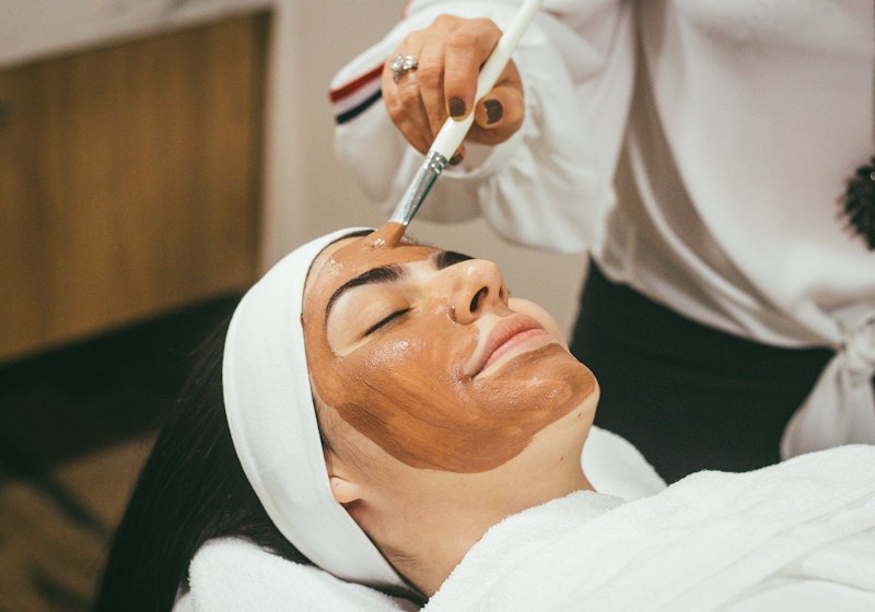 A clay mask being brushed on during a facial, towels tucked around.